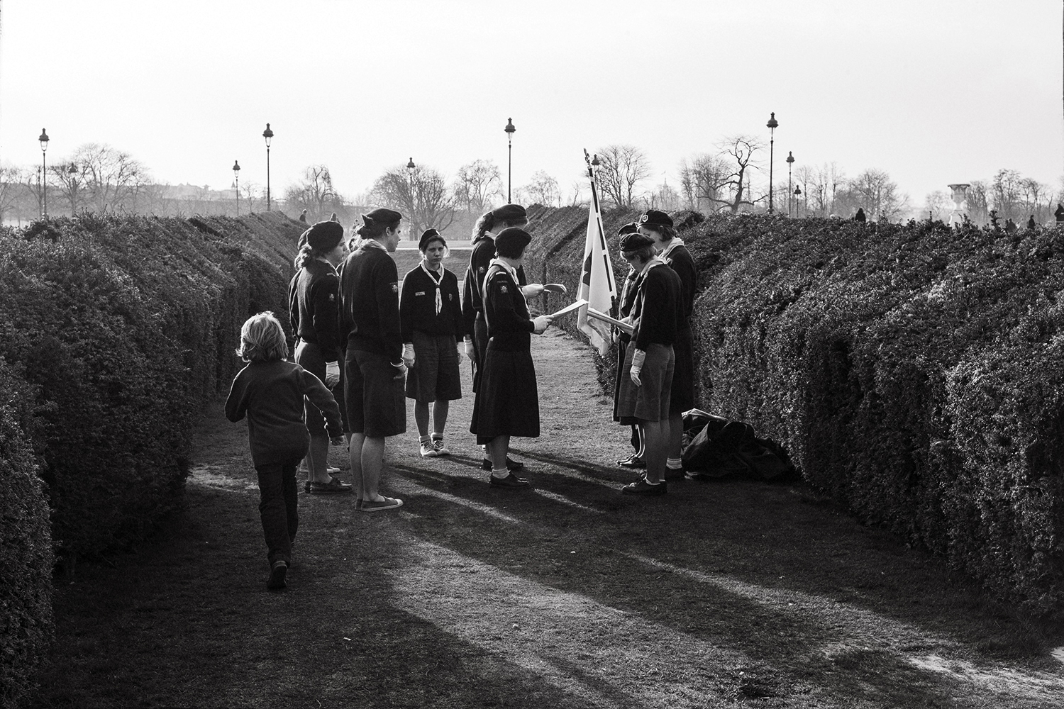 When To Make Street Photography? A young girl runs past a group of girl guides performing a small ceremony in the Tuillerie gardens in Paris