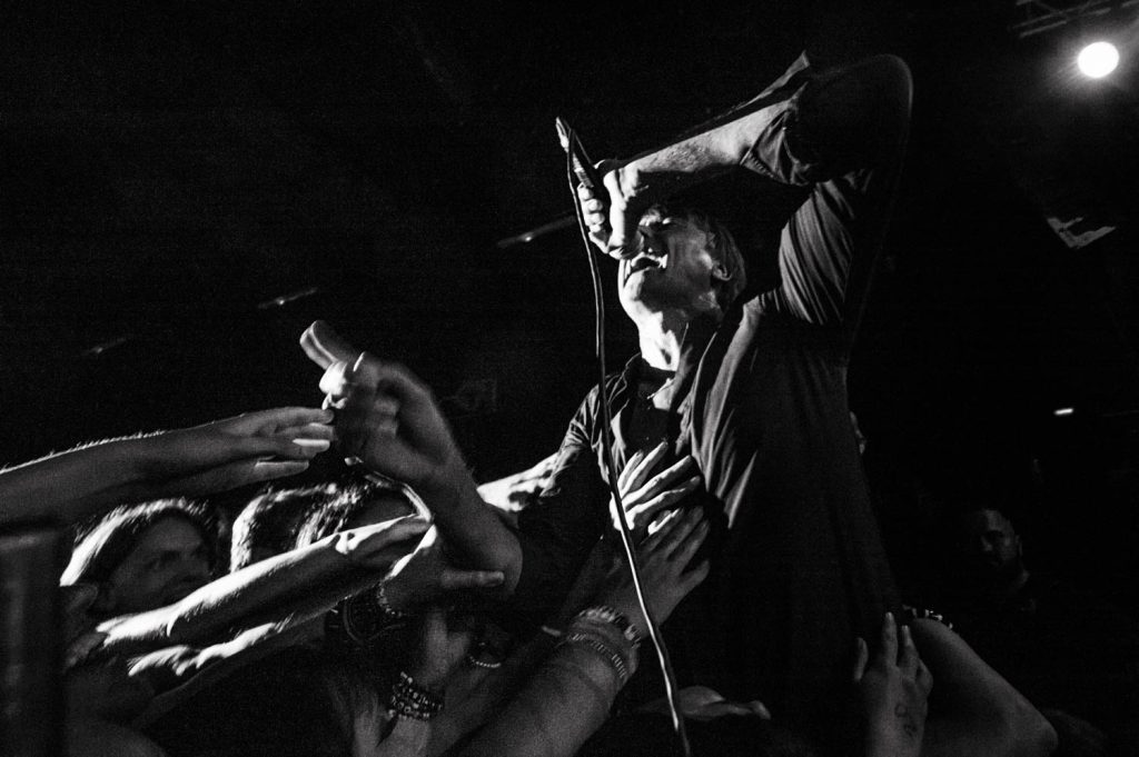 Concert image of Suede's Brett Anderson singing next to the audience