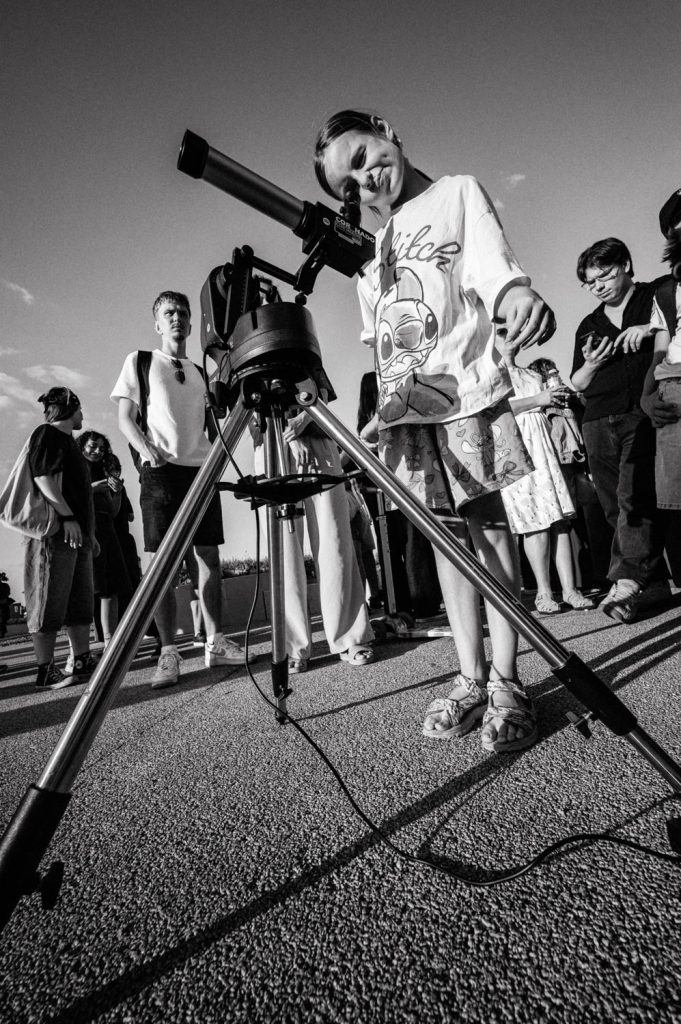 A young girl squints as she views the partial eclipse through a telescope.